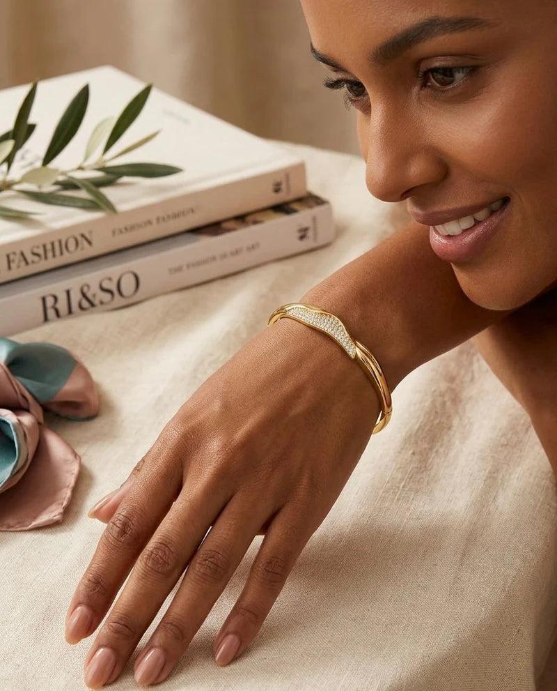 Woman's hand wearing a gold bracelet with fashion magazines and sunglasses in the background