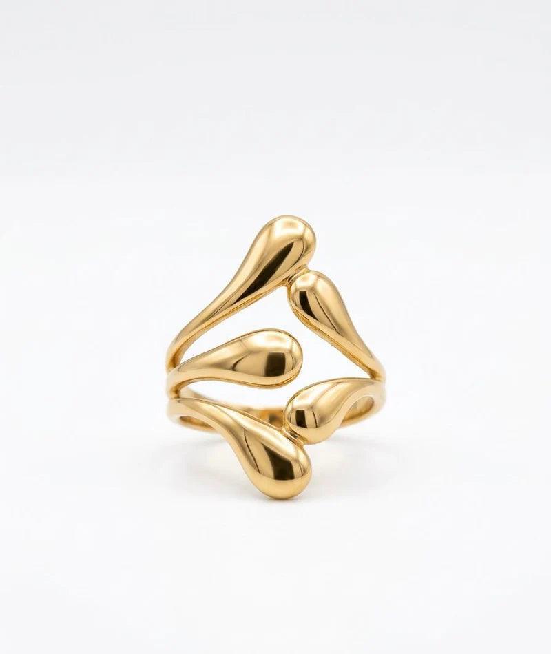A gold-plated open ring with a fluid, organic wavy design resembling dripping wax or droplets, photographed on a seamless white background.