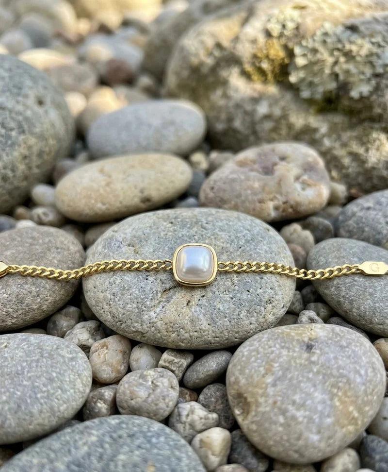 Gold bracelet with a pearl-like bead on pebbles