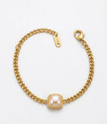 A gold chain bracelet featuring a central square bezel-set pearl, photographed on a clean white background.