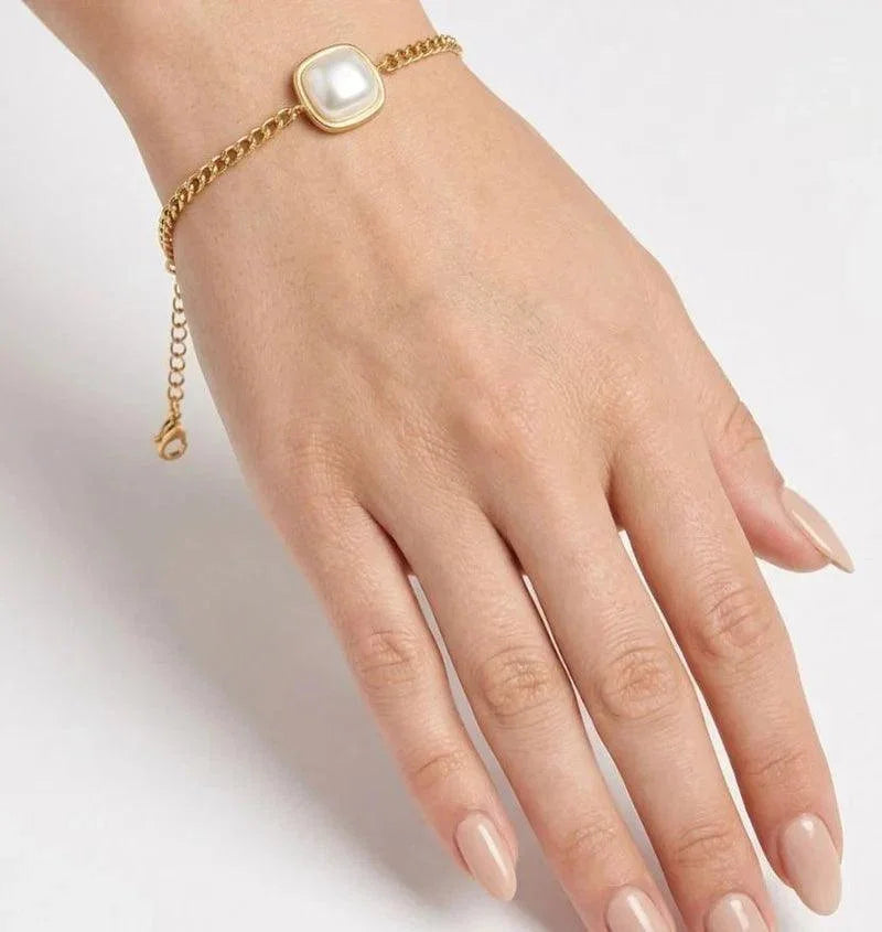 A gold chain bracelet with a square white faux-pearl centerpiece, shown worn on a woman's wrist against a clean white background.