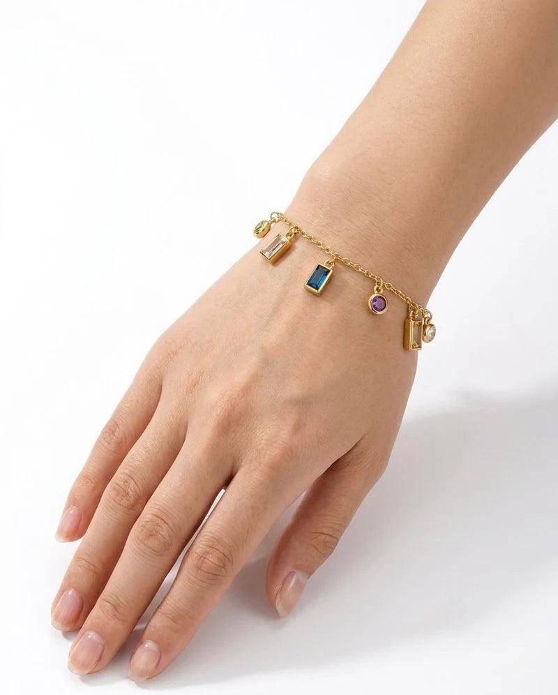 Gold bracelet with colorful charms on a hand against a white background