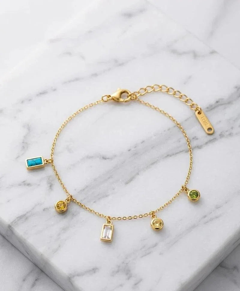 Gold bracelet with various charms on a marble surface