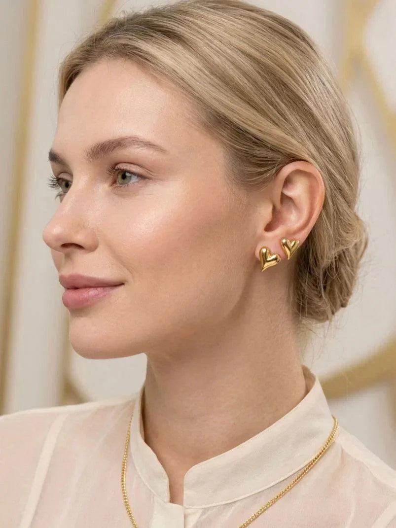 Woman wearing gold heart-shaped earrings with a blurred background