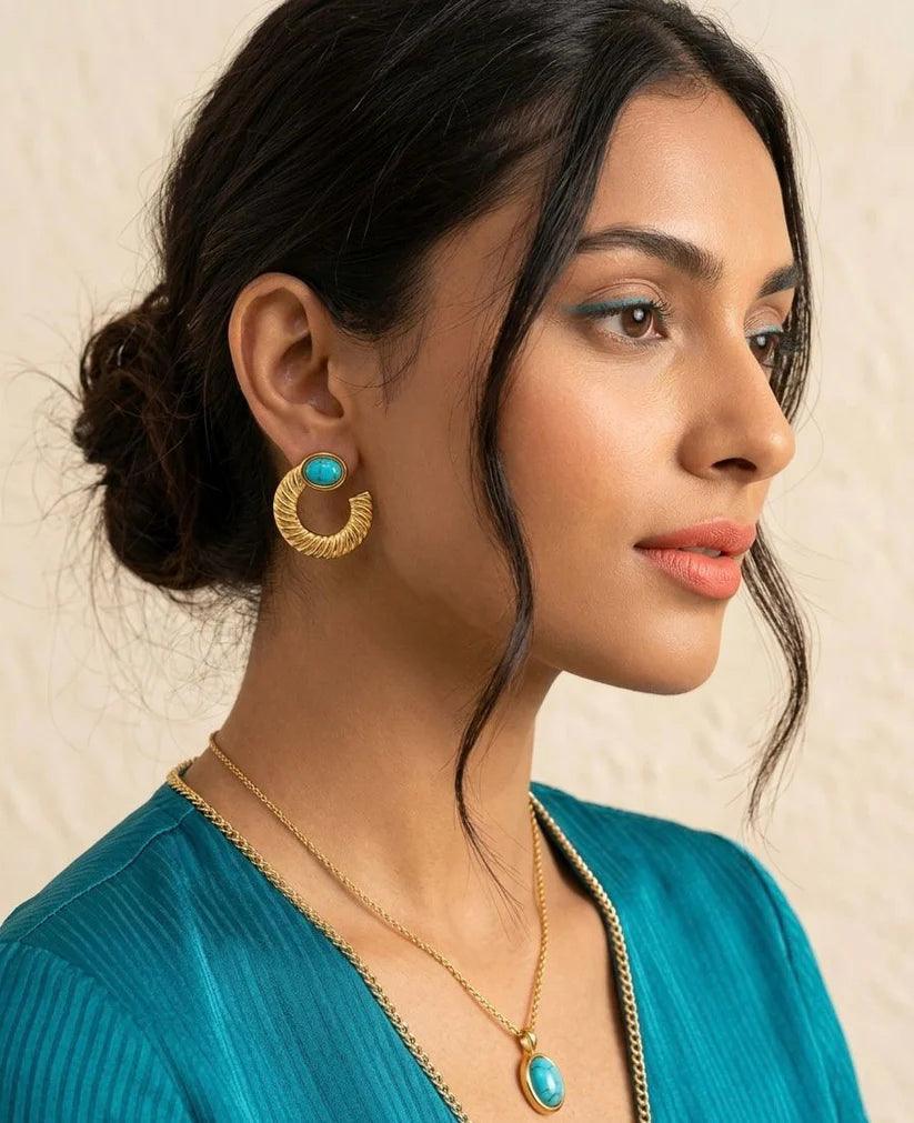 Woman wearing gold earrings and necklace with turquoise stones against a beige background