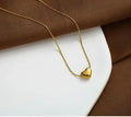 A delicate gold chain necklace with a small, polished gold heart pendant, styled on a white plate with brown fabric in the background.