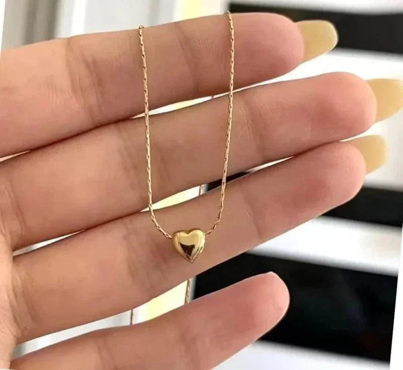 Gold heart-shaped necklace held between fingers against a blurred background