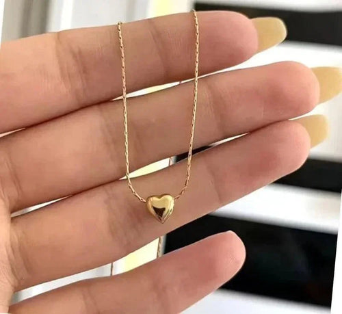 Gold heart-shaped necklace held between fingers against a blurred background
