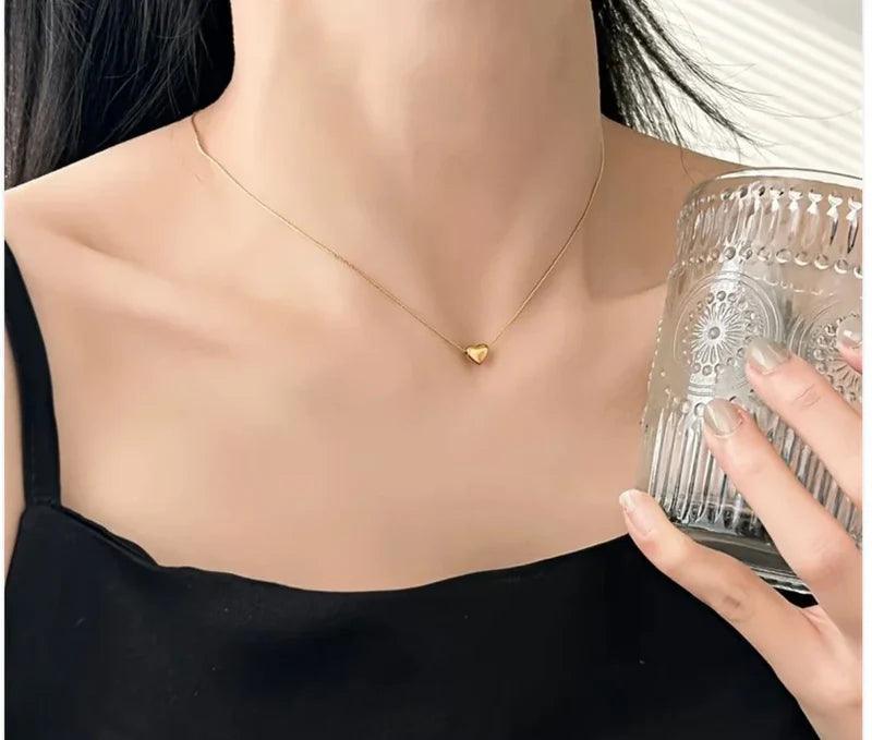 Person wearing a gold necklace with a heart pendant, holding a glass container.