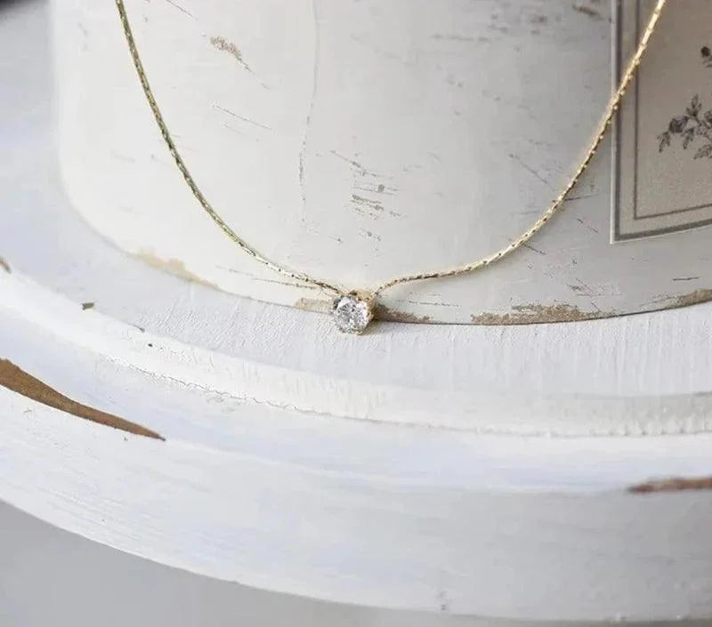 Delicate gold necklace with a small round pendant on a white surface