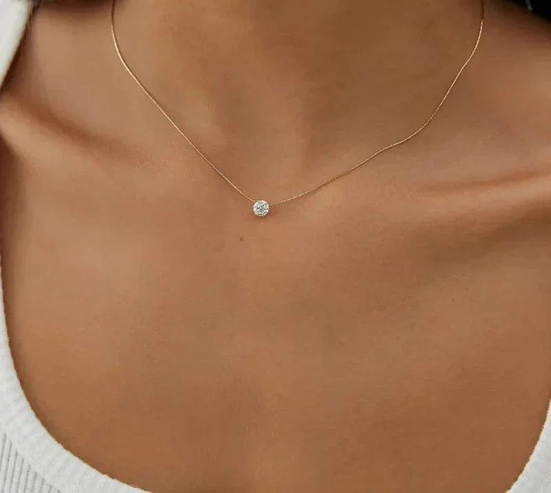 Gold necklace with a small round pendant on a person wearing a white top.