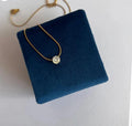 Gold necklace with a diamond pendant on a blue cushion