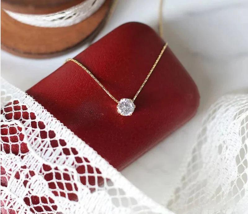 Gold necklace with a diamond pendant on a red box, surrounded by lace and leather.