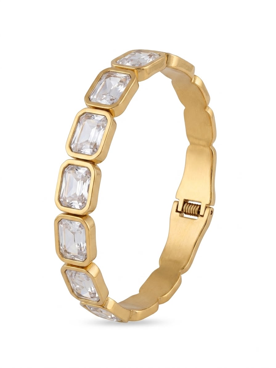 A gold bangle bracelet featuring a row of rectangular clear crystals in gold bezel settings, shown on a plain white background.