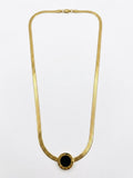 A gold snake chain necklace with a circular black onyx pendant, displayed against a plain white background.
