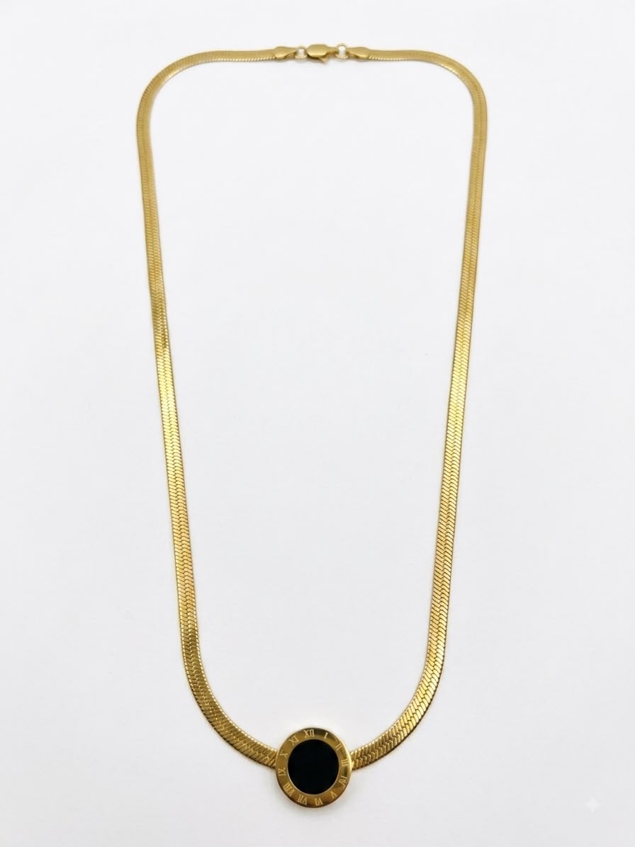 A gold snake chain necklace with a circular black onyx pendant, displayed against a plain white background.