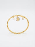 A gold-toned bangle bracelet with a bamboo-inspired segmented design, featuring three hanging charms: a white pearl, a round gold charm with a teddy bear motif surrounded by small clear stones, and a small clear stone charm, set against a plain white background.