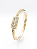 A gold bangle bracelet with a rectangular bezel-set diamond centerpiece and rows of small diamonds along the band, displayed on a clear stand against a white background.