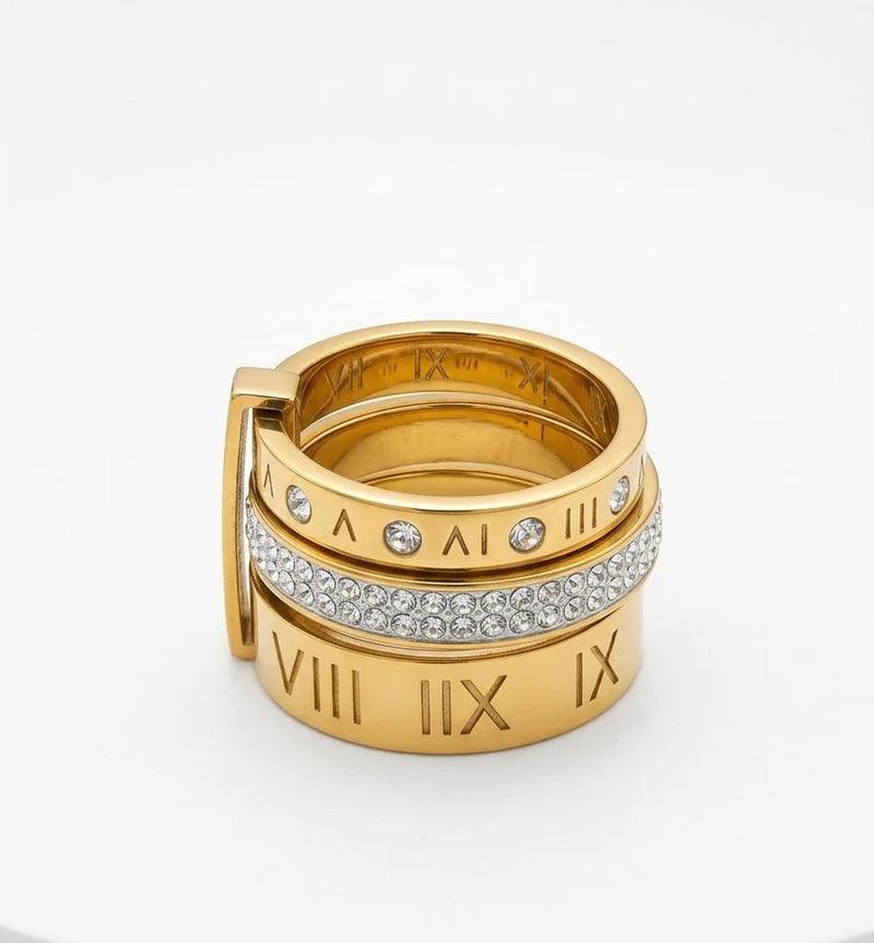 A gold-tone stack ring set featuring Roman numerals (VIII, IX, X) engraved on the bands, with one band adorned in a row of clear pavé stones, photographed on a clean white background.