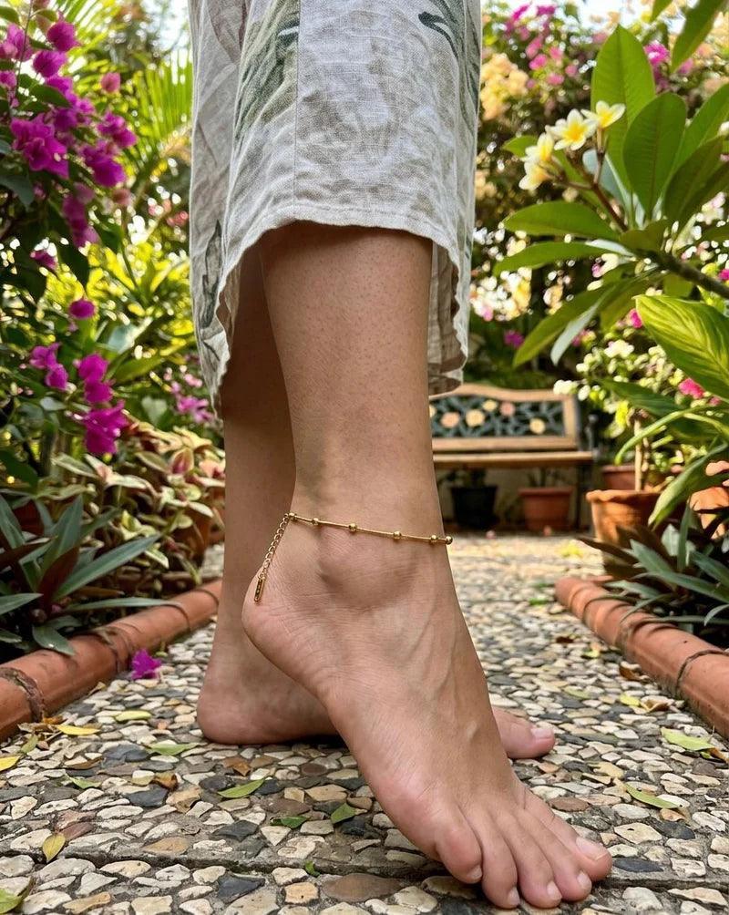Person wearing a gold anklet with a garden background