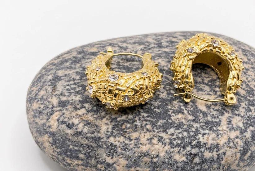 Gold hoop earrings with embedded stones on a textured stone surface