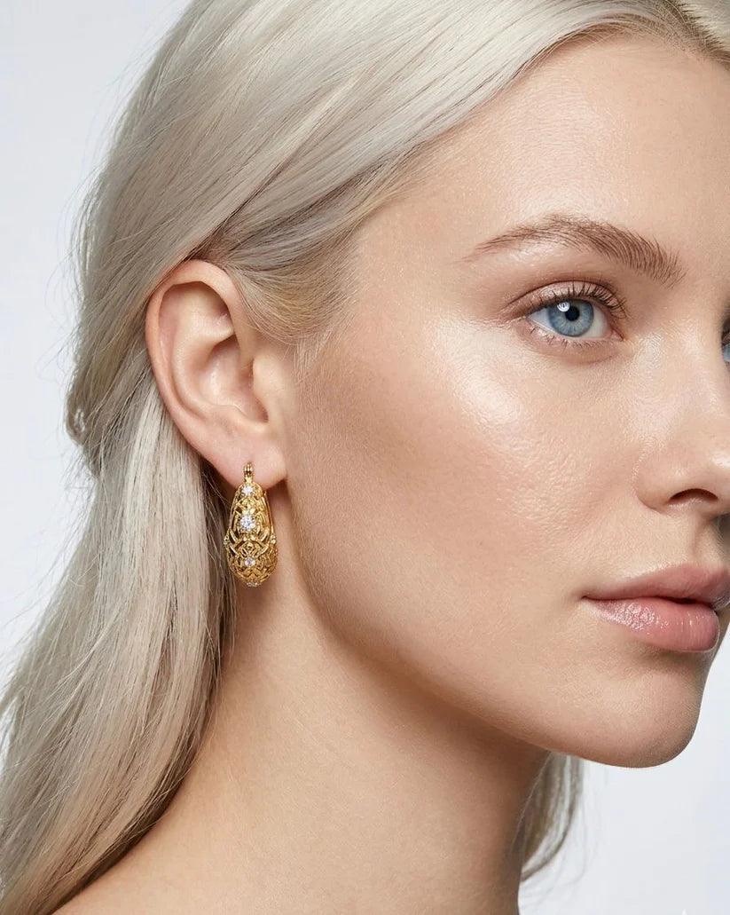 Close-up of a woman wearing gold hoop earrings with a plain background