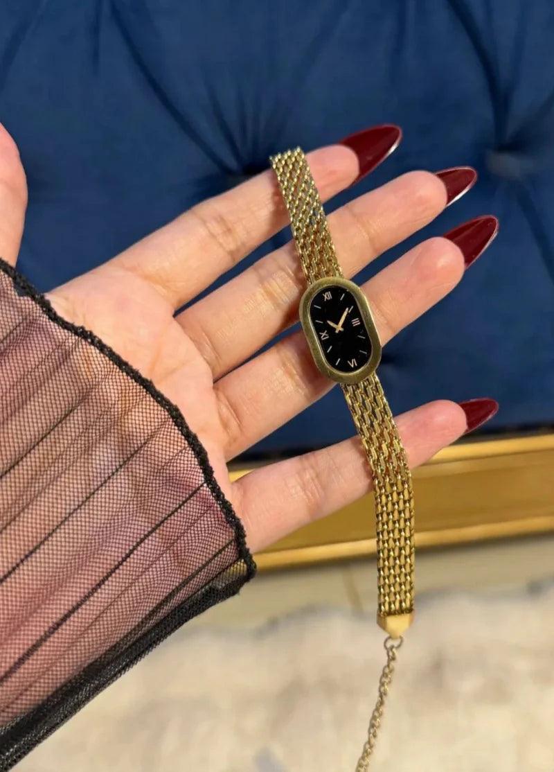 Gold watch with a black face held in a hand against a blue background