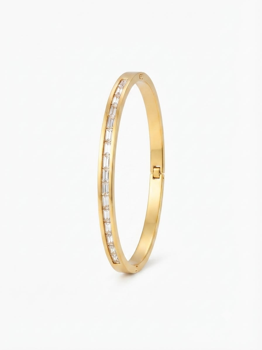 A slim gold bangle bracelet featuring a channel-set row of clear baguette-cut stones along one side, shown on a clean white background.