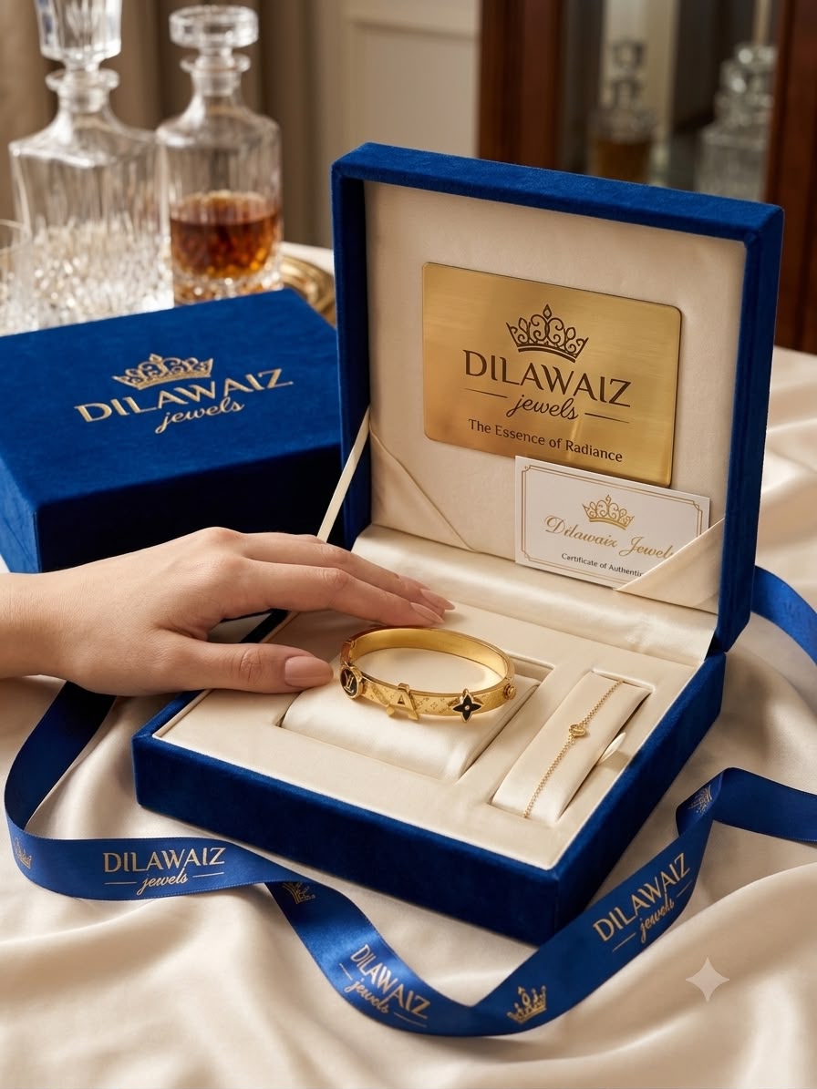 A gold bangle bracelet with floral motifs is displayed inside an open blue velvet jewelry box branded Dilawaiz Jewels, with a hand reaching toward it. A matching blue box and ribbon are visible in the background on a draped cream fabric surface.