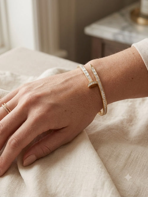 A close-up of a person's hand and wrist wearing a slim gold cuff bracelet with pavé-set clear stones, resting on a textured cream linen surface.