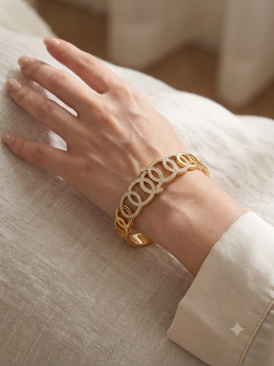 A gold-toned bangle bracelet with interlocking circular links, worn on a person's wrist over a light beige fabric surface.