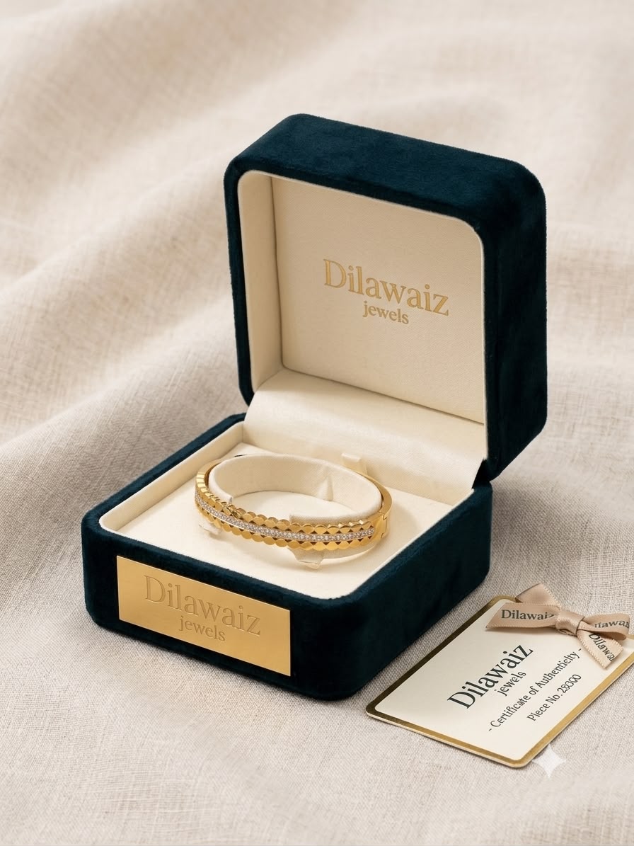 A gold double-band ring with pavé-set clear stones displayed in an open dark teal velvet jewelry box on a beige fabric background. A branded Dilawaiz jewelry certificate card is placed beside the box.