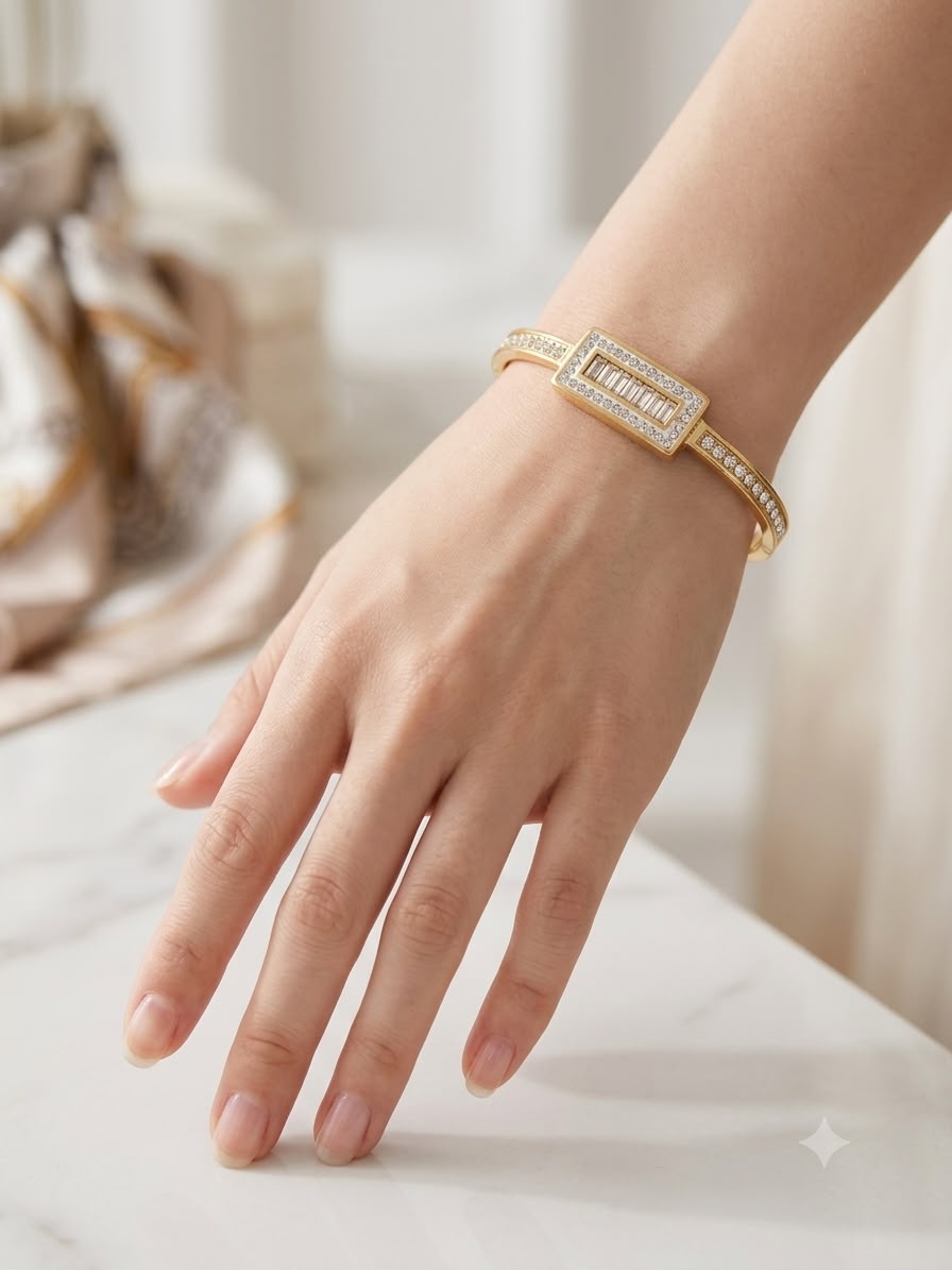 A gold bangle bracelet with a rectangular pavé center and side channel stones, shown worn on a woman's wrist over a light marble surface.