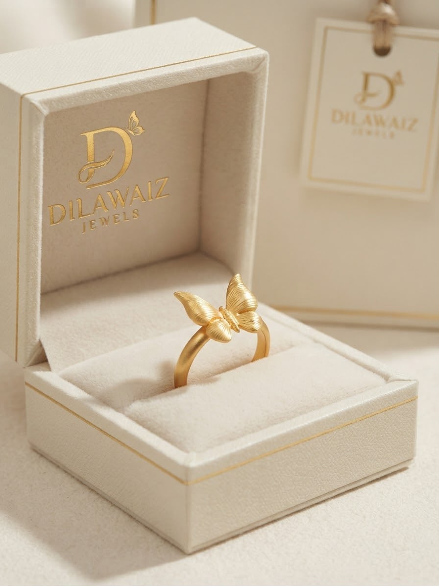 A gold butterfly ring displayed in an open cream-colored jewelry box with the brand name 'Dilawaiz Jewels' printed inside. A matching branded tag hangs in the background.