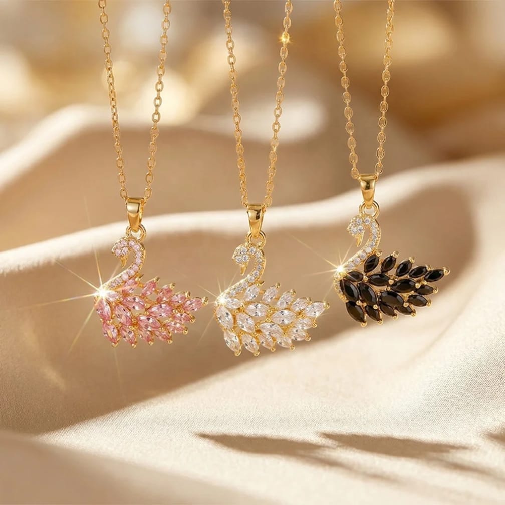 Three gold necklaces with swan pendants on a beige fabric background