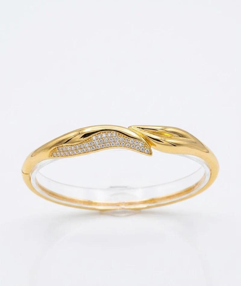 A gold ring with a twisted, leaf-like design featuring a pavé-set row of small clear stones on one side, shown on a clean white background.