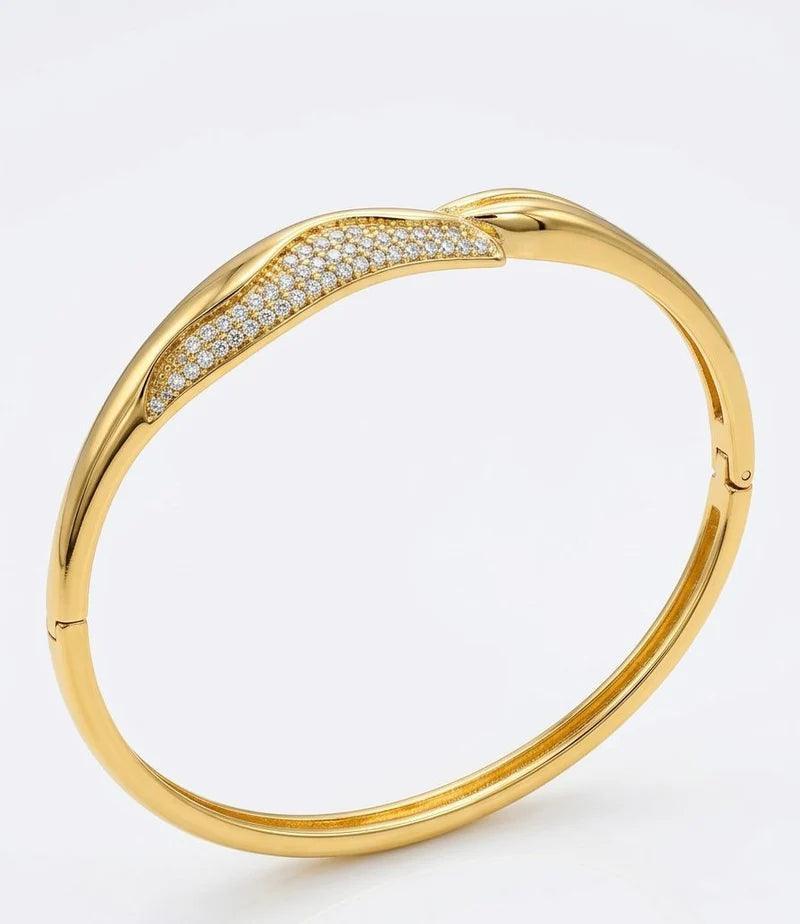 A polished gold bangle bracelet featuring a pavé-set row of clear stones along the upper curve, shown on a clean white background.